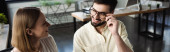 Smiling manager touching eyeglasses while talking to intern in office, banner  mug #617177324