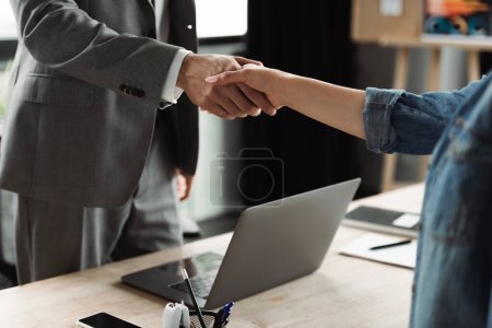 Photo for Cropped view of job seeker and businessman shaking hands near devices in office - Royalty Free Image