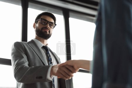 Vista de ángulo bajo del hombre de negocios en traje estrechando la mano del buscador de empleo en la oficina 