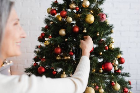 mujer de mediana edad borrosa y alegre con pelo gris decorando el árbol de Navidad 