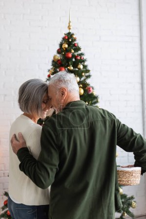 smiling middle aged couple hugging while decorating christmas tree