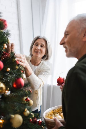 cheerful middle aged couple decorating christmas tree with baubles
