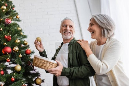 positive middle aged woman hugging husband decorating christmas tree