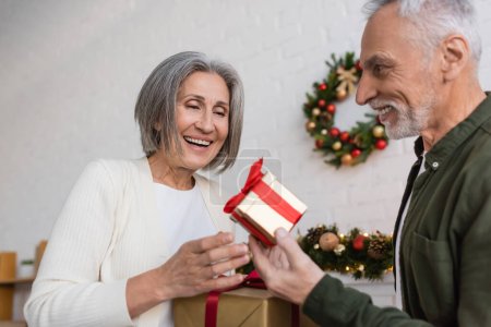 Téléchargez les photos : Heureux homme d'âge moyen tenant cadeau de Noël près de femme gaie - en image libre de droit