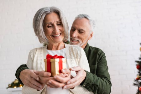 cheerful mature man and happy woman holding christmas present in hands