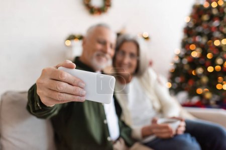 middle aged man taking selfie with wife near christmas tree on blurred background 
