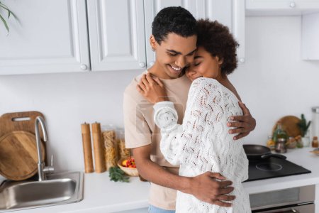 fröhliches afrikanisch-amerikanisches Paar, das sich in der Küche in der Nähe der Arbeitsplatte umarmt