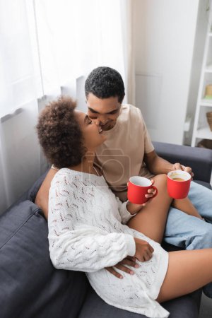 Foto de Vista de ángulo alto de la pareja afroamericana con copas rojas sonriendo en el sofá en casa - Imagen libre de derechos