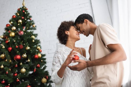 Téléchargez les photos : Vue à angle bas du couple afro-américain debout face à face avec les yeux fermés près de l'arbre de Noël à la maison - en image libre de droit