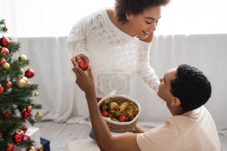 young african american couple smiling at each other near wicker basket with christmas balls