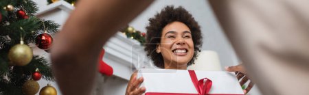 vue à faible angle de rire femme afro-américaine avec Noël présent près de copain flou, bannière