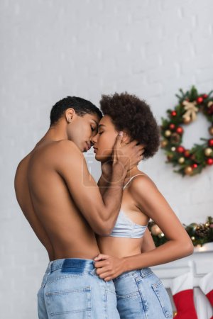 Téléchargez les photos : Homme musclé torse nu embrassant séduisante copine afro-américaine près floue couronne de Noël - en image libre de droit