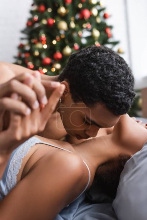 jeune homme afro-américain tenant la main avec sa petite amie et embrassant son cou sur le premier plan flou