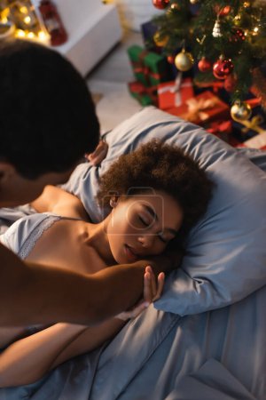 Foto de Vista de ángulo alto de la mujer afroamericana con los ojos cerrados haciendo el amor con novio borroso en la víspera de Navidad - Imagen libre de derechos