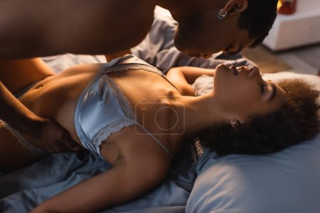 young african american man over passionate woman in silk bra on bed