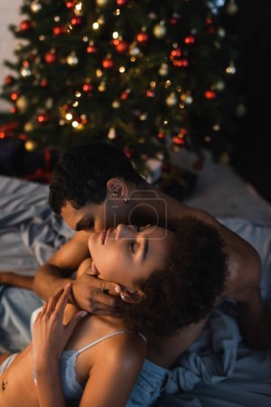 homme afro-américain étreignant le cou et embrassant femme séduisante avec les yeux fermés 
