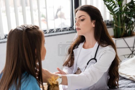 Photo for Doctor in white coat checking neck of child in hospital ward - Royalty Free Image