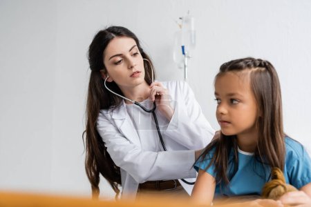 Pediatrician with stethoscope checking back of patient in hospital ward 