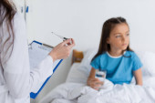 Doctor holding thermometer and clipboard near blurred child with glass of water in clinic  Sweatshirt #620101476