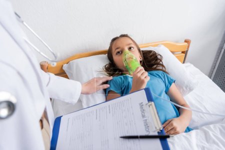 Foto de Médico sosteniendo máscara de oxígeno y portapapeles cerca del paciente en la cama del hospital - Imagen libre de derechos