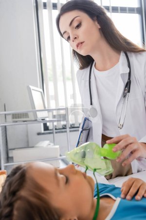 Kinderarzt hält Sauerstoffmaske in der Hand und betrachtet Patientin in Klinik 