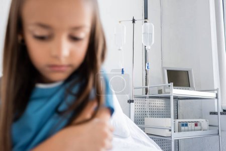 Intravenous therapy on stand near blurred child in patient gown in clinic 