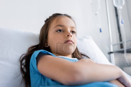 Low angle view of sad kid lying on bed in hospital ward 