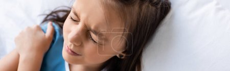 Photo for High angle view of ill child touching shoulder while lying on bed in hospital ward, banner - Royalty Free Image