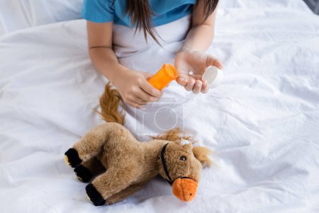 Foto de Vista recortada de niños sosteniendo píldoras cerca de juguete en la cama en la clínica - Imagen libre de derechos