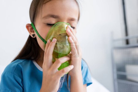 Niño enfermo en bata de paciente usando máscara de oxígeno en la clínica 