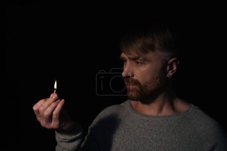 man looking at flame of burning match during energy blackout isolated on black