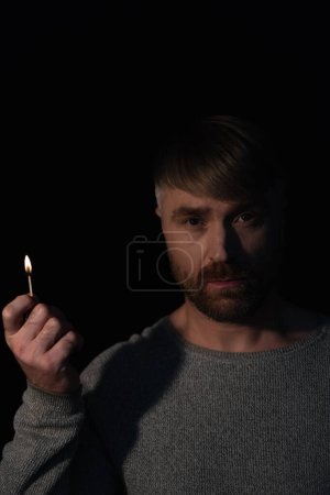 Foto de Hombre con fuego partido mirando a la cámara durante el apagado de la electricidad aislado en negro - Imagen libre de derechos