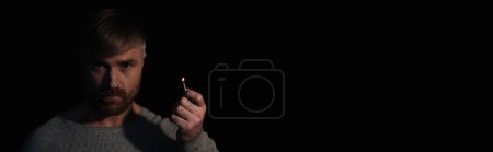 man looking at camera while holding lit match during power outage isolated on black, banner