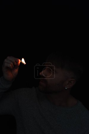 man looking at flame of burning match during power outage isolated on black