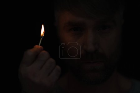 close up view of man holding lit match and looking at camera isolated on black