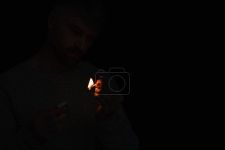 Mann mit Streichholzschachtel sieht brennendes Streichholz bei Stromausfall isoliert auf schwarz