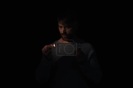 Téléchargez les photos : Homme tenant allumette brûlante et ampoule pendant l'arrêt de l'électricité isolé sur noir - en image libre de droit
