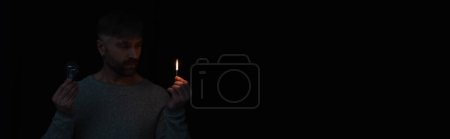 Mann während Stromabschaltung hält brennendes Streichholz und Glühbirne isoliert auf schwarz, Banner