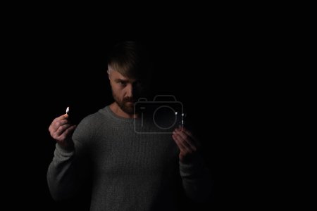 Irritierter Mann mit Glühbirne und brennendem Streichholz blickt isoliert auf schwarze Kamera