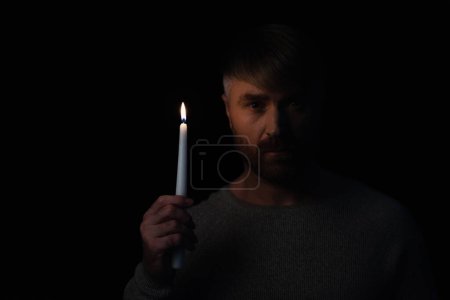 Mann mit brennender Kerze bei Stromausfall und Blick in Kamera isoliert auf schwarz