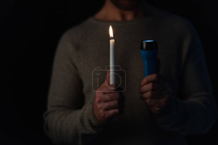 partial view of blurred man with burning candle and flashlight isolated on black