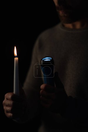 abgeschnittene Ansicht des Mannes mit Taschenlampe und brennender Kerze isoliert auf schwarz