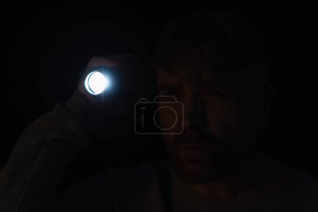 Mann mit heller Taschenlampe schaut in der Dunkelheit isoliert auf schwarz weg