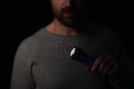 abgeschnittene Ansicht des Mannes mit glühender Taschenlampe während der Stromabschaltung isoliert auf schwarz