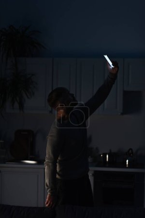 Photo pour Man searching for mobile connection while standing with smartphone in raised hand during power shutdown - image libre de droit