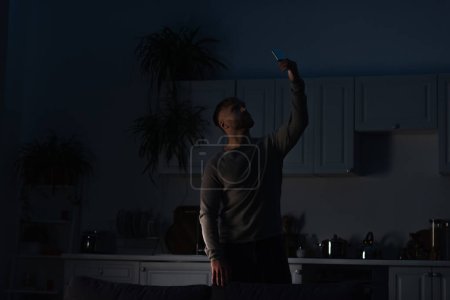 Mann hält Smartphone in erhobener Hand auf der Suche nach Verbindung bei Stromausfall