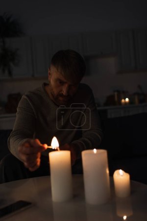 man sitting in dark kitchen during power outage and lighting candles