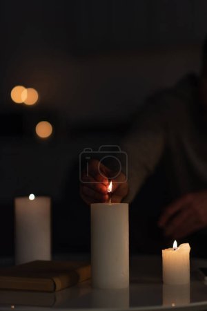 Téléchargez les photos : Vue recadrée de l'homme allumant des bougies dans l'obscurité causée par l'arrêt de l'électricité - en image libre de droit