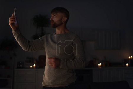 hombre con teléfono celular de pie en la oscuridad y la búsqueda de la señal móvil durante el apagón de energía