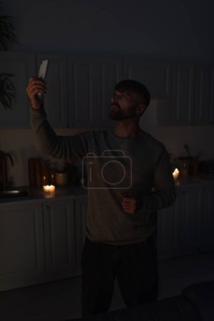 hombre de pie con teléfono inteligente en la mano levantada mientras busca la señal móvil durante el apagado de la electricidad